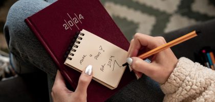 Woman writing future plans in a 2024 planner with focus on personal goals and organization.