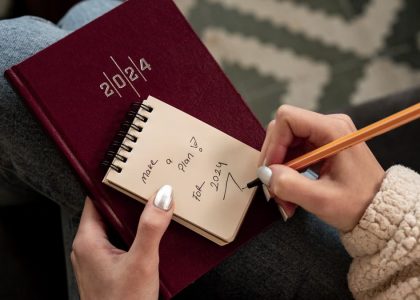 Woman writing future plans in a 2024 planner with focus on personal goals and organization.